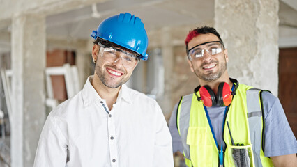 Two men builder and architect smiling confident standing together at construction site