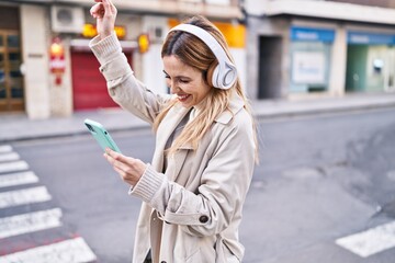 Fototapeta premium Young blonde woman listening to music and dancing at street