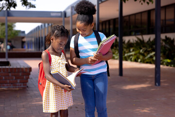 Happy african american schoolchildren holding notebooks and spending time in school yard