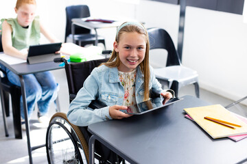 Portrait of happy caucasian schoolgirl in wheelchair with diverse schoolchildren in school classroom