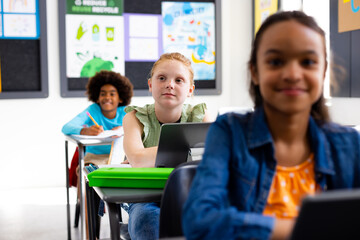 Happy diverse schoolchildren sitting at desks in school classroom