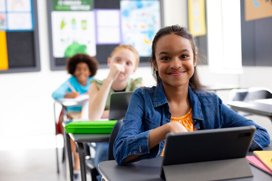 Happy diverse schoolchildren sitting at desks in school classroom