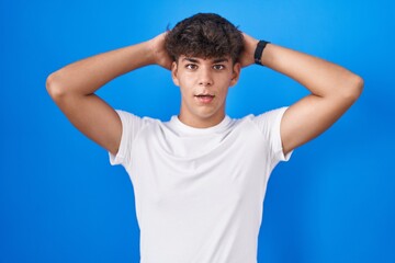 Hispanic teenager standing over blue background crazy and scared with hands on head, afraid and surprised of shock with open mouth