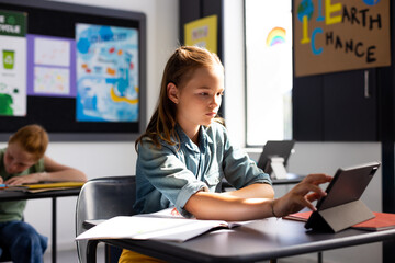 Caucasian schoolgirl sitting at desk and using tablet in school classroom