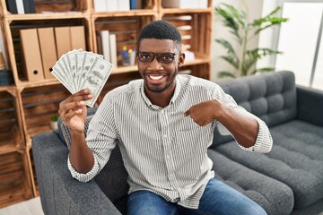 African american man holding dollars pointing finger to one self smiling happy and proud