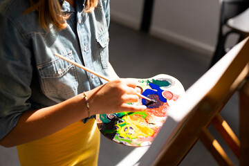 Fototapeta premium Happy caucasian schoolgirl painting using brush and easel in school art class