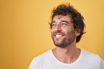 Obraz premium Young hispanic man smiling confident looking to the side over isolated yellow background