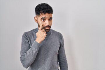 Hispanic man with beard standing over white background pointing to the eye watching you gesture, suspicious expression