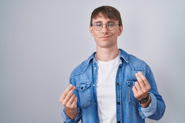 Caucasian blond man standing wearing glasses doing money gesture with hands, asking for salary payment, millionaire business