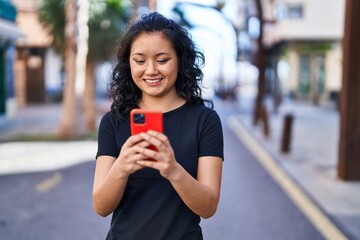 Young chinese woman smiling confident using smartphone at street