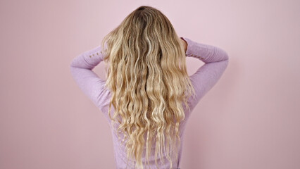 Young blonde woman touching her hair backwards over isolated pink background
