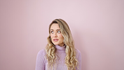 Young blonde woman looking to the side with serious expression over isolated pink background