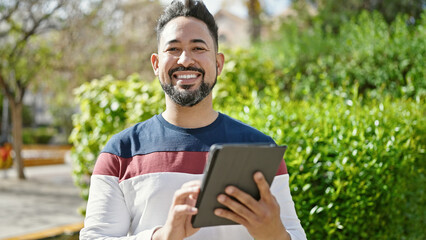 Fototapeta premium Young latin man smiling confident using touchpad at park