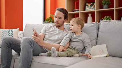 Father and son using smartphone sitting on sofa together at home