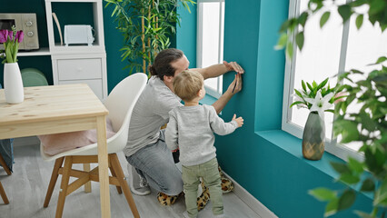 Father and son measuring child on wall at dinning room