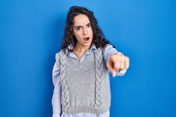 Young brunette woman standing over blue background pointing displeased and frustrated to the camera, angry and furious with you