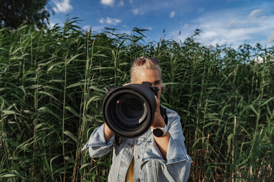 A beautiful girl photographer with a professional camera with a large telephoto lens takes a photo in nature.
