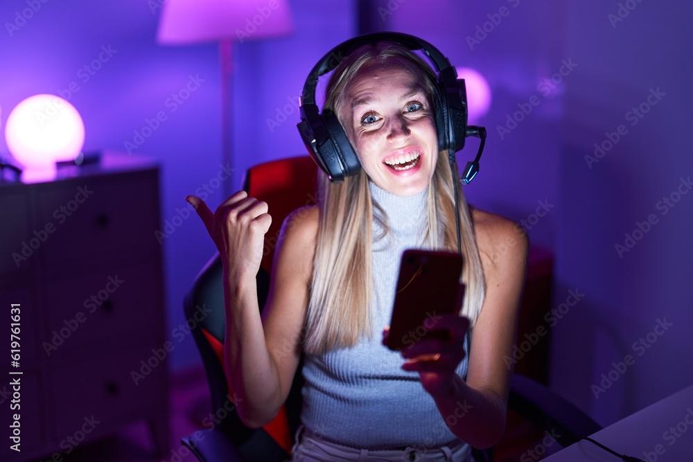 Sticker Young caucasian woman playing video games with smartphone pointing thumb up to the side smiling happy with open mouth