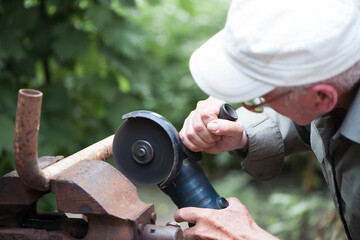 old man working. Cutting a metal pipe. spark. the pipe is clamped in a vice. man's hands hold a...