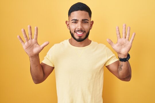 Young hispanic man standing over yellow background showing and pointing up with fingers number ten while smiling confident and happy.
