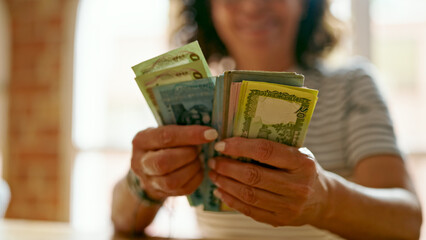 Middle age hispanic woman counting bangladesh taka banknotes at home