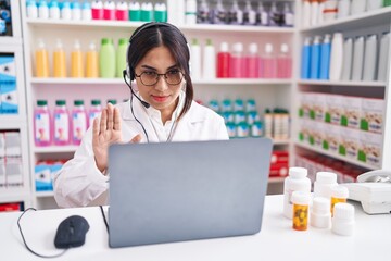 Young arab woman working at pharmacy drugstore using laptop doing stop sing with palm of the hand. warning expression with negative and serious gesture on the face.