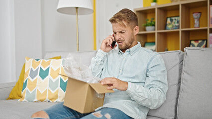 Young caucasian man speaking on the phone unpacking cardboard box at home
