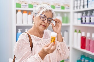 Middle age grey-haired woman customer reading pills label at pharmacy