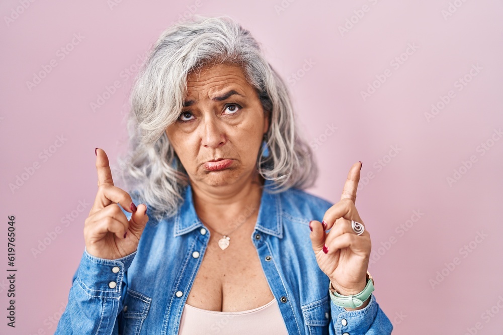 Canvas Prints Middle age woman with grey hair standing over pink background pointing up looking sad and upset, indicating direction with fingers, unhappy and depressed.