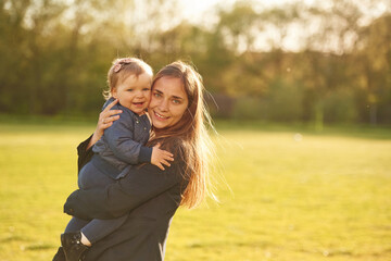 Fototapeta premium Mother is holding her little daughter in hands on the summer field