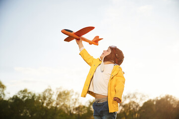 In yellow colored jacket. Little boy is playing with toy plane on the summer field