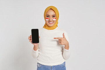 Smiling Happy young Asian Muslim woman pointing a finger at the display mobile phone blank screen, recommends apps isolated over white background. Celebrate Indonesian independence day on 17 August