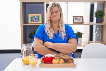 Obraz na płótnie Canvas Caucasian plus size woman eating breakfast at home skeptic and nervous, disapproving expression on face with crossed arms. negative person.