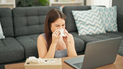 Young beautiful hispanic woman using laptop sneezing at home