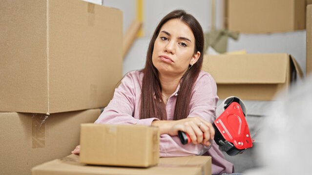 Young Beautiful Hispanic Woman Packing Cardboard Box With Sad Expression At New Home