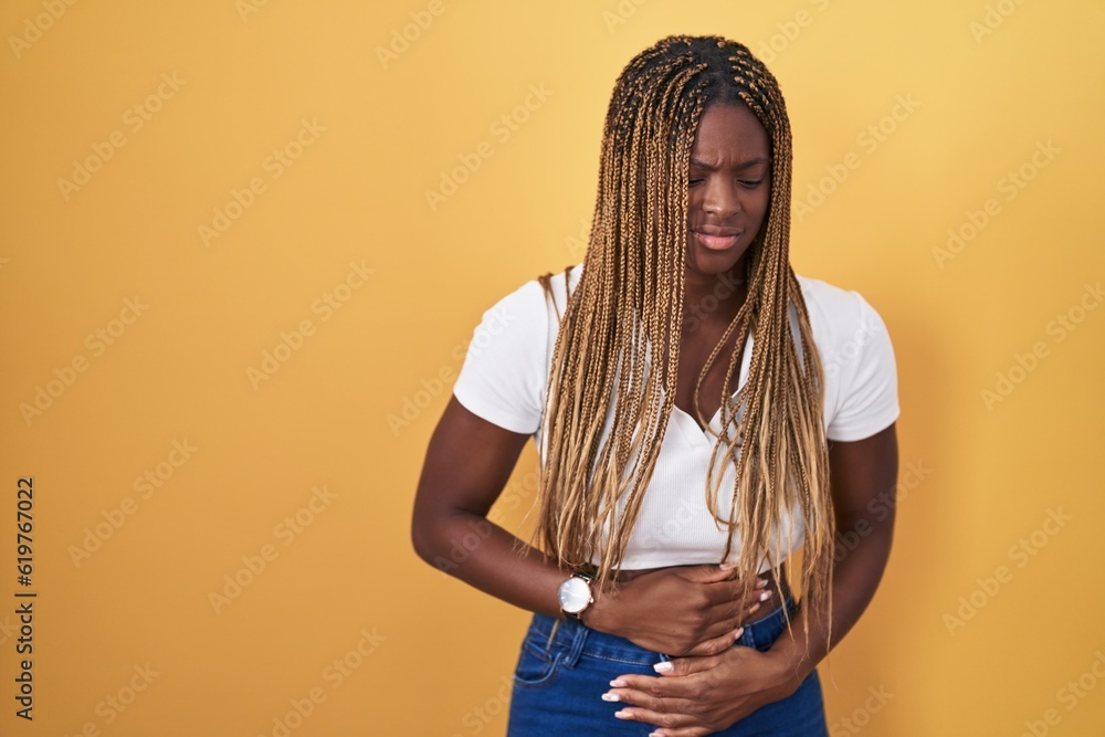 Sticker African american woman with braided hair standing over yellow background with hand on stomach because indigestion, painful illness feeling unwell. ache concept.