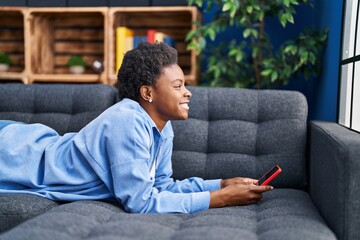 African american woman using smartphone lying on sofa at home
