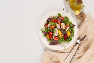 Salad with chicken, mango, strawberries and green leaves on a white background