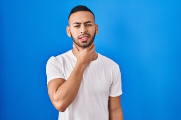 Young hispanic man standing over blue background touching painful neck, sore throat for flu, clod and infection