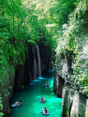 Naklejka premium Under fresh greenery, people enjoy boating at Takachiho Gorge, a famous tourist attraction in Miyazaki Prefecture, Japan