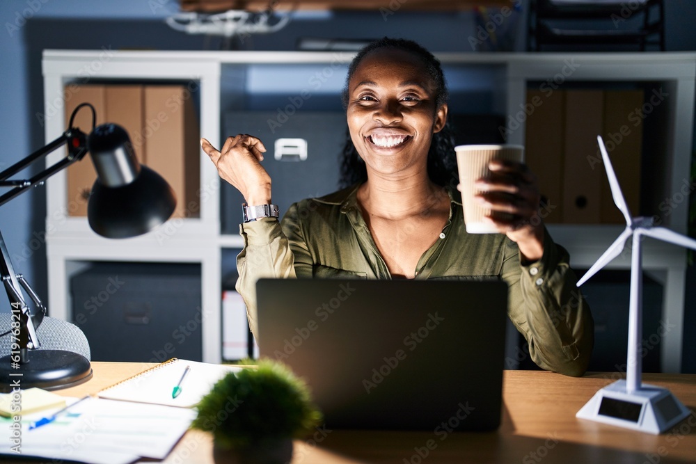 Canvas Prints african woman working using computer laptop at night with a big smile on face, pointing with hand fi