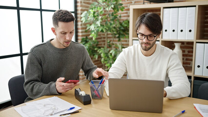 Two men business partners using laptop and smartphone working at office