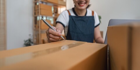 Young Asian business woman working at warehouse preparing SME package box for delivery at small business home