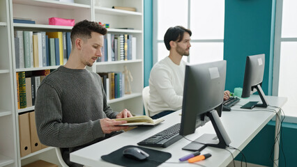 Two men students using computer reading book studying at library university