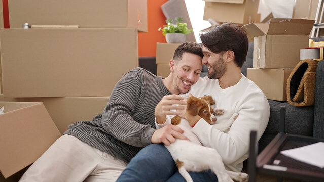 Two men couple smiling confident sitting on floor hugging dog at new home - Powered by Adobe