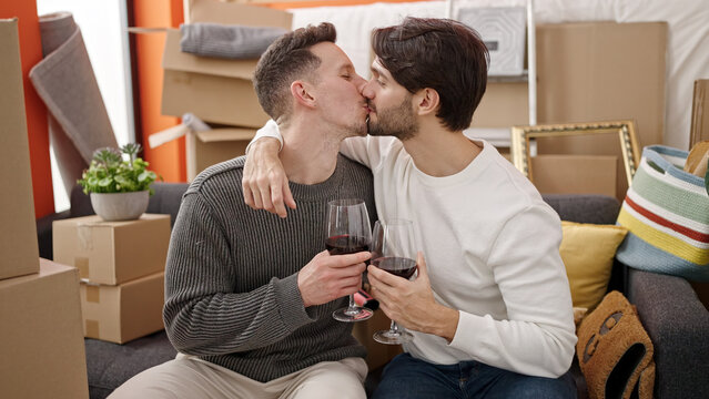 Two men couple drinking glass of wine kissing at new home