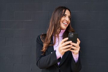 Young hispanic woman smiling confident using smartphone over black background