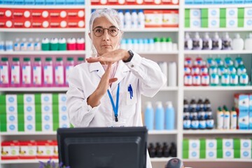 Middle age woman with tattoos working at pharmacy drugstore doing time out gesture with hands,...