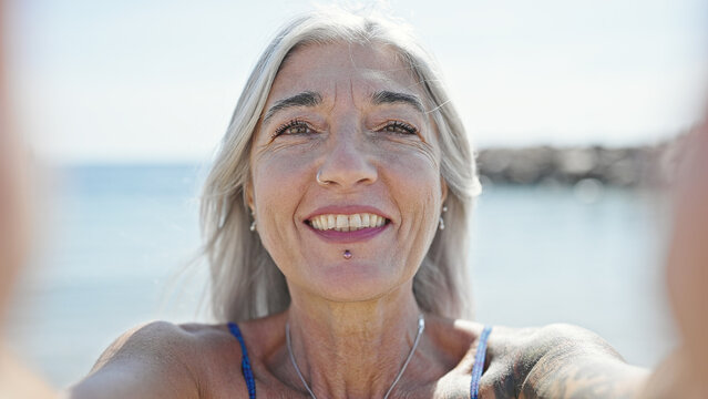 Middle age grey-haired woman tourist make selfie by camera at beach