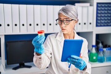 Middle age grey-haired woman scientist using touchpad holding test tube at laboratory